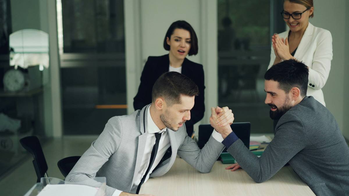 Bearded young people office workers are having fun practising arm wrestling while attractive women are watching and supporting them then doing high-five and clapping hands.