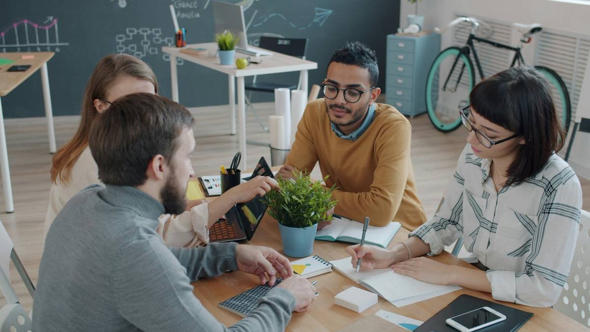 Joyful colleagues mixed race men and women are talking at desk in office then doing high-five and laughing. Collaboration, people and business concept.